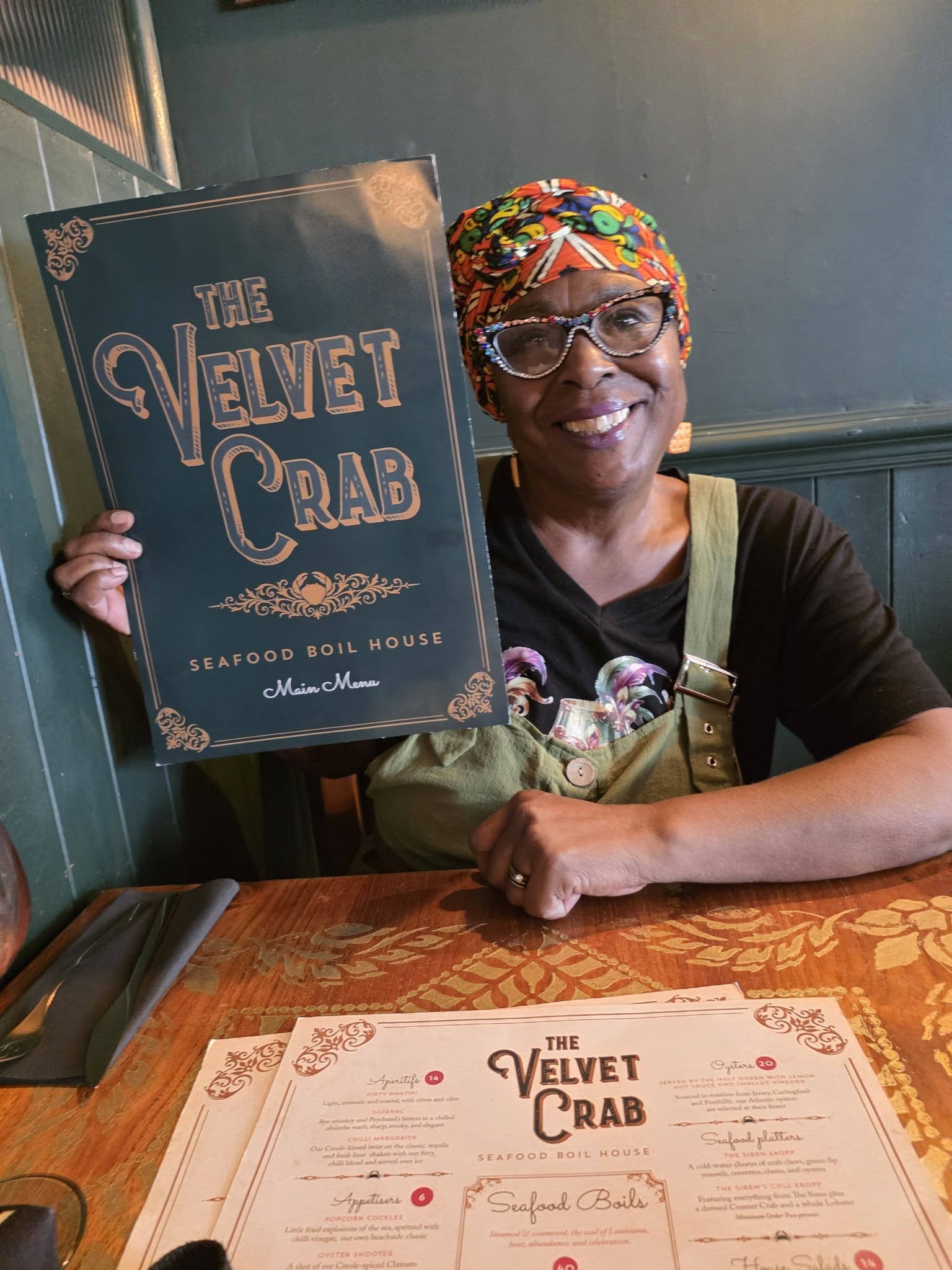 Momma Cherri holding The Velvet Crab menu in the restaurant