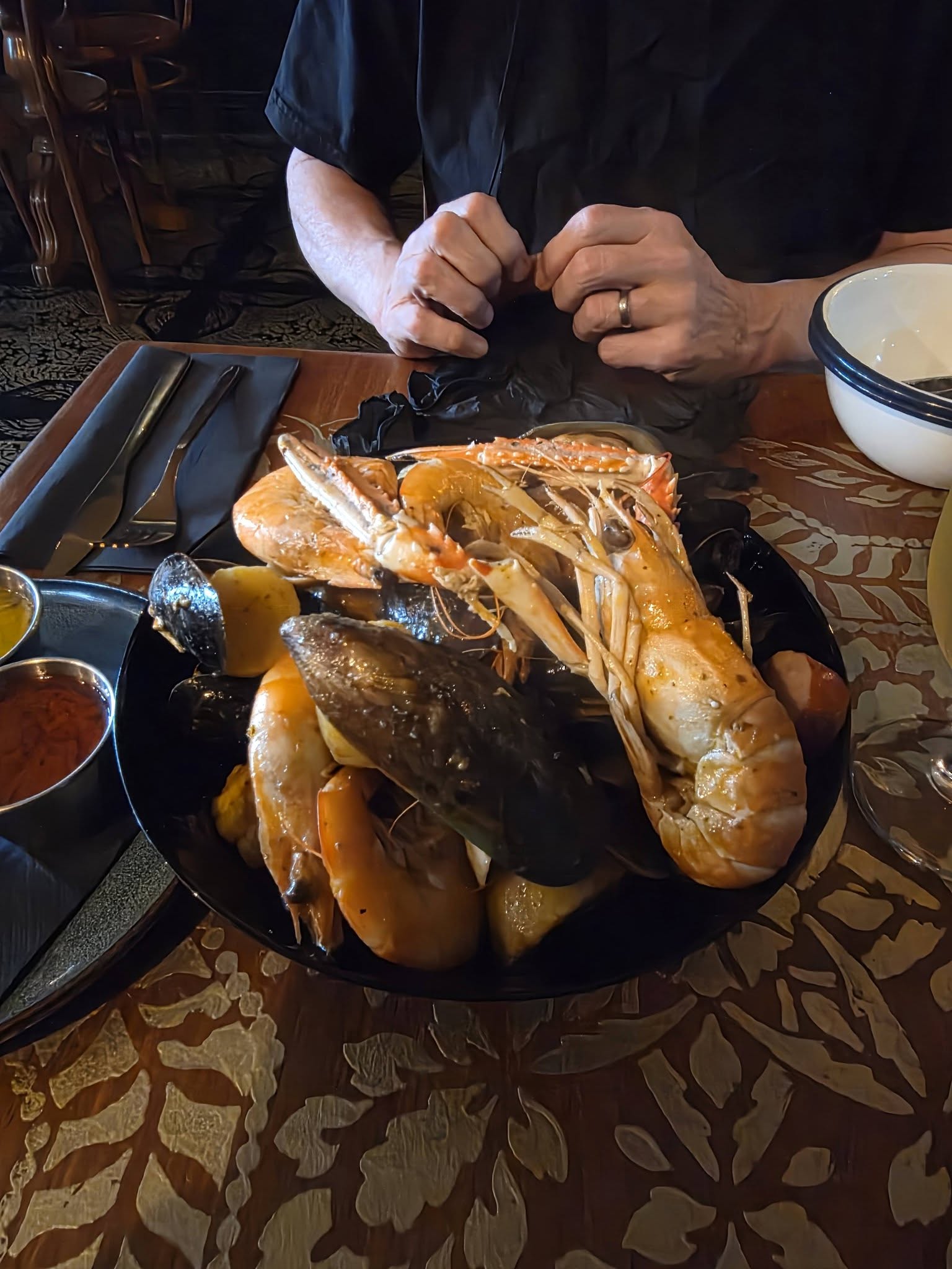 Seafood boil with prawns and mussels, hands reaching in with gloves